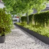A garden path with gravel, bordered by black edging and lush greenery, with trees and a building in the background. Náhled obrázku produktu