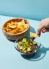 A hand is dipping a tortilla chip into a bowl of black bean dip with avocado and corn. Produktbild-Vorschau
