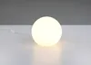 A white spherical lamp with a power cord and switch is placed on a white surface against a gray background. Produktbild-Vorschau