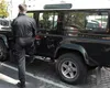 A person in a black jumpsuit is stepping into a black SUV. Náhled obrázku produktu