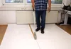 A person is using a tape dispenser to apply tape to a large roll of white paper on the floor. Produktbild-Vorschau