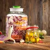 A large glass fermenting jar filled with red cabbage, carrots, and cauliflower, next to a smaller jar of pickled items, on a wooden table. Anteprima dell’immagine prodotto