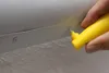 A hand is using a yellow tool to make a hole in a metal strip. Produktbild-Vorschau