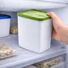 A hand is placing a white freezer container with a green lid into a freezer. Produktbild-Vorschau