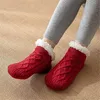 Rote Zopfmuster-Hausschuhe-Socken mit weißem Kunstfellfutter, getragen von einer Person in grauen Leggings auf strukturiertem braunen Boden Náhľad obrázku produktu