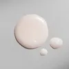 Three drops of a light pink liquid product on a light gray background. Anteprima dell’immagine prodotto