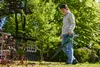 A person is using a leaf blower in a garden with a shed in the background. Náhľad obrázku produktu