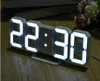 A digital clock with LED display sits on a wooden surface, with flowers in the background. Produktbild-Vorschau
