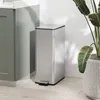 A silver trash can with a foot pedal is placed next to a green cabinet and a potted plant. Podgląd zdjęcia produktu