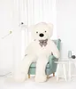 A large white teddy bear is sitting in a light blue armchair in a room with white curtains and a white rug. Produktbild-Vorschau