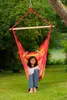 A woman is relaxing in a colorful hammock chair hanging from a tree in a grassy yard. Produktbild-Vorschau
