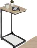 A C-shaped side table with a light wood top and black metal frame, shown against a white background. A coffee mug, a small potted plant, and a notebook with a phone on top are placed on the table. Produktbild-Vorschau