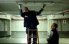Two men are in a parking garage. One man is on a ladder, working on a light fixture. The other man is standing below, holding a flat object. Podgląd zdjęcia produktu