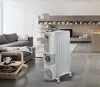 A white oil-filled radiator is placed in a modern living room next to a gray sofa and a coffee table. Náhľad obrázku produktu