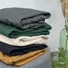 A stack of folded bedding in various colors, with a decorative vase and dried grass in the background. Produktbild-Vorschau