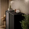 A close-up view of a black dresser with decorative items on top, set against a textured wall and curtains. Produktbild-Vorschau