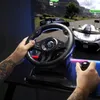 A person is playing a racing game using a steering wheel and pedals, with the game displayed on a large screen in the background. Anteprima dell’immagine prodotto
