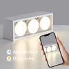 A hand holds a smartphone displaying a reflection of a white LED ceiling light fixture with three lamps. The fixture is on a white surface, with a grey background. Text overlays indicate 'Augenschutz' (eye protection) and 'Flimmerfrei' (flicker-free). Produktbild-Vorschau