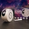 A star projector lamp and its packaging are displayed on a dark surface with a starry night sky background. Podgląd zdjęcia produktu