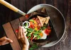 A breakfast spread is being prepared on a wooden surface, with hands arranging vegetables. Produktbild-Vorschau
