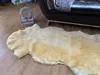 A sheepskin rug is laid out on a wooden floor next to a dark leather sofa. Produktbild-Vorschau