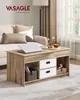 A living room scene with a coffee table in the foreground, featuring a laptop, decorative items, and storage drawers, next to a sofa and window. Produktbild-Vorschau