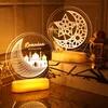 Two illuminated Ramadan-themed acrylic night lights are displayed on a surface with books and a decorative lantern. Produktbild-Vorschau