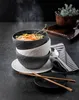A stack of three textured bowls, one filled with steaming soup, sits on a dark surface next to a striped napkin and cutlery. Produktbild-Vorschau