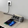 A power strip with multiple outlets and USB ports is shown charging two smartphones on a wooden desk, plugged into a wall socket. Produktbild-Vorschau
