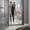 A woman is holding a child and walking through a doorway with a baby gate. Voir les images du produit