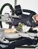 A close-up shot of a miter saw cutting a piece of wood, with a hand operating the saw. Podgląd zdjęcia produktu