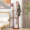 A coat rack with shelves is shown next to a bed, with a painting on the wall and a plant in the background. Náhľad obrázku produktu