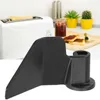 A black bread maker paddle is shown in the foreground, with a blurred background of a kitchen scene including a toaster, jam, and plants. Produktbild-Vorschau