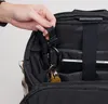 A hand is shown attaching a carabiner with keys to a loop inside a black backpack. Produktbild-Vorschau