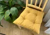A yellow seat cushion on a wooden chair next to a large green plant. Produktbild-Vorschau