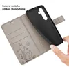 A hand is holding a black phone case over an open gray wallet case with card slots and a floral design. Produktbild-Vorschau