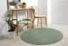 A round green rug is placed on a light wooden floor in front of a console table with a plant and decorative items. Produktbild-Vorschau