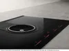 A close-up, angled view of a modern black induction cooktop with an integrated ventilation system. Náhled obrázku produktu
