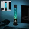 A PlayStation-themed lava lamp is shown on a desk next to a computer monitor and headphones, with a smaller inset image showing the lamp in an 'OFF' state. Podgląd zdjęcia produktu