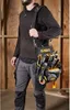 A person wearing work clothes and a tool bag is standing in a workshop. Anteprima dell’immagine prodotto