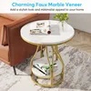 A round side table with a faux marble top and gold metal legs, placed next to a brown leather sofa on a rug. Produktbild-Vorschau