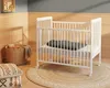 A nursery room with a white crib, a basket of baby items, and decorative pillows on a rug. Anteprima dell’immagine prodotto