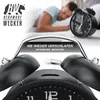 A man sleeping in bed next to an alarm clock, with a close-up of the alarm clock in the foreground. Produktbild-Vorschau