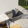 An outdoor sink with a faucet mounted on a wall next to a countertop, with a tiled patio and grass in the background. Produktbild-Vorschau