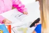 Two people are at a table, one is reading a book and the other is holding a scanning pen over a map. Produktbild-Vorschau