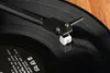 A close-up of a turntable's tonearm and cartridge resting on a vinyl record. Anteprima dell’immagine prodotto