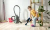 A young boy is playing with a toy vacuum cleaner next to a real vacuum cleaner, a broom, and a bucket. Produktbild-Vorschau