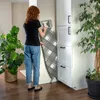 A woman is standing next to a tall white cabinet, holding a folded ironing board. Produktbild-Vorschau