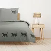 A bed with a duvet cover and pillowcase featuring a cat silhouette pattern, placed in a bedroom setting with a nightstand and lamp. Produktbild-Vorschau