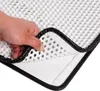 A hand is shown lifting a corner of a white cat litter mat with a black border, revealing its layered structure. Produktbild-Vorschau